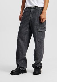 Sorte denim cargo bukser med løs pasform, der har sidelommer, kontrastsyninger og en let slidt finish.
