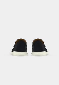 Svart kanvas slip-on sko med en kremfarget gummisåle, rund tå og et enkelt design. Innvendig foret med brunt tekstil.