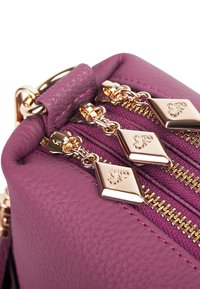 Lila Lederhandtasche mit goldenen Beschlägen, ausgestattet mit drei Reißverschlussöffnungen und dekorativen Reißverschlussanhängern in Diamantform mit gravierten Details.