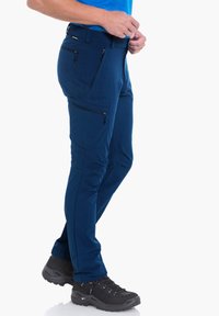 Herren Outdoor-Hosen in Blau aus leichtem, strapazierfähigem Material mit Reißverschlusstaschen, tapered Fit und verstärkten Knien; kombiniert mit strukturierten schwarzen Wanderschuhen.