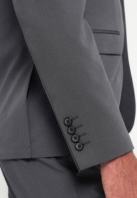 Dark gray suit jacket sleeve with a smooth texture, featuring four black buttons and stitching detail along the cuff.