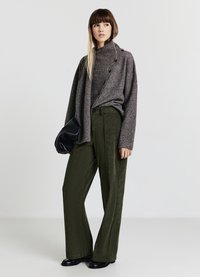 Cardigan gris avec boutons, superposé à un haut assorti, et associé à un pantalon large en velours côtelé vert olive. Tient une pochette noire texturée.