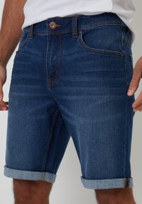 Shorts in denim blu scuro con orlo risvoltato. Caratteristiche includono cinque tasche, passanti per cintura e cuciture a contrasto. Texture liscia.