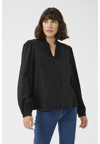 Chemisier noir à boutons avec un col texturé, des manches bouffantes et une coupe légèrement ample. Le tissu semble lisse et léger.