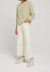 Chemise à manches longues rayée beige et blanche, associée à un jean blanc à jambes larges et des baskets beige clair. Design simple avec une coupe décontractée.