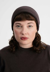 Donkergrijze gebreide beanie op een persoon met schouderlang krullend haar. Ze dragen een bijpassende donker trui met een ronde hals.