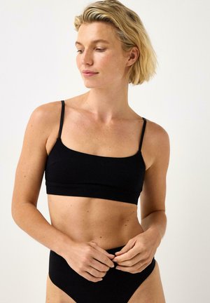 Svart kort bralette med tunna axelband, tillverkad av slät tyg. Den har en enkel fyrkantig halsringning och en figurnära design.