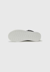 Sneaker con una toma in tessuto testurizzato con un motivo scuro, una suola in gomma bianca e un battistrada dettagliato per la trazione. Forma piatta e arrotondata.