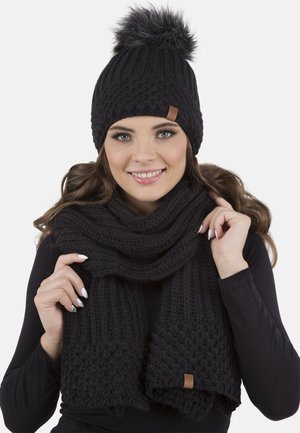 Berretto di lana nera a maglia con pon-pon in pelliccia sintetica, abbinato a una sciarpa spessa a maglia dello stesso colore, entrambi con un design testurizzato e un'etichetta in cuoio.