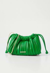 Pequena bolsa de cordão verde em couro com um design pregueado e alça de corrente dourada, repousando sobre uma superfície branca.