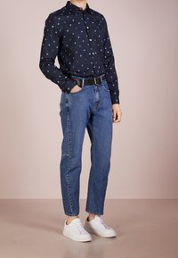 Marinblå knapp-up skjorta med cirkelformade mönster, tillsammans med ljusblå jeans och vita sneakers. Har ett flerfärgat randigt bälte.