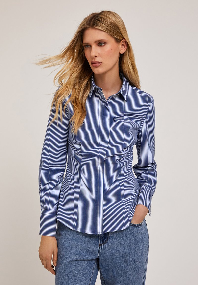 Niebieska i biała koszula w paski z wywiniętym kołnierzykiem, długimi rękawami i dopasowanym krojem, wykonana z lekkiego materiału o gładkiej fakturze.