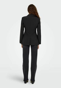 Must mustriga bleiser, millel on nurgeline krae, kitsas lõige ja seljal üks lõhik, koos tumedate kitsaste pükstega. Sile tekstuur.