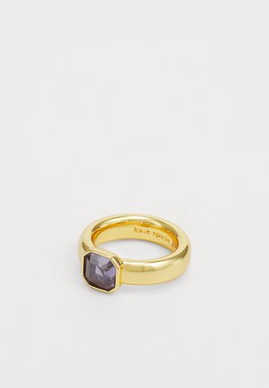 Gold-tone ring featuring a faceted octagonal purple stone set in a smooth band. Engraved branding visible inside the band.