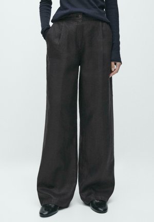 Weit geschnittene Hosen aus dunkelbraunem Stoff, mit Knopfverschluss, zwei Seitentaschen und glatter Textur. Kombiniert mit einem enganliegenden Oberteil.