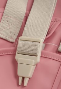 Detail van een roze rugzak met een beige band met een gestructureerde afwerking, plastic gesp en stiksels. Achtergrond van glad materiaal.