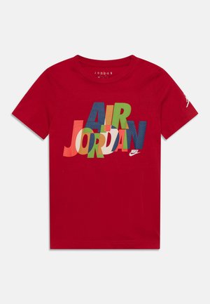 T-shirt en coton rouge avec un imprimé coloré portant les mots "AIR JORDAN". Manches courtes et col rond.