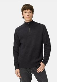 Schwarzer, gerippter Strickpullover mit hohem Kragen und halbem Reißverschluss, in entspannter Passform und mit langen Ärmeln. Tragen mit dunklen Jeans.