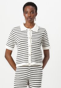 Kortermet, svart og hvitstripet strikket cardigan med krage og knappelukking, som har et strukturert, vevd stoff.