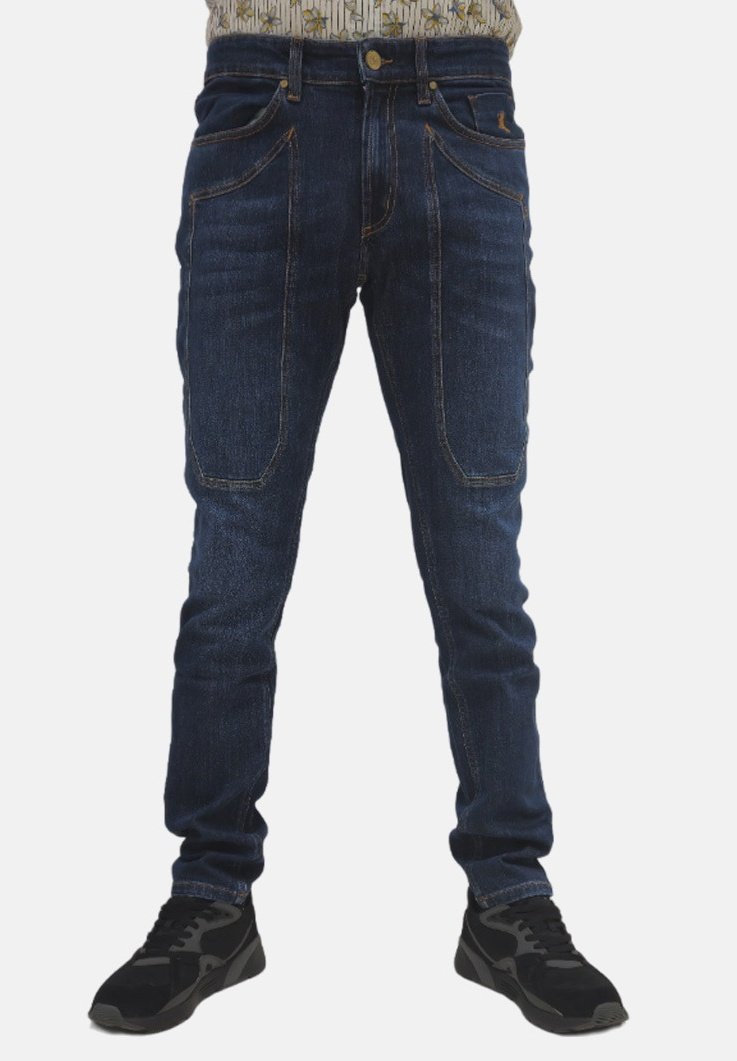 Jeans in denim blu scuro con design aderente, cinque tasche e cuciture arancioni a contrasto. Indossati con scarpe da ginnastica nere.