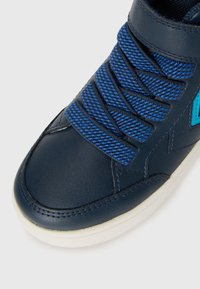 Donkerblauwe sneaker met dikke, gestructureerde blauwe veters, witte zool en blauwe stoffen details aan de zijkant.