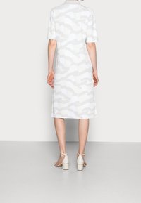 Witte jurk met korte mouwen, met een golvend patroon in lichtgrijs. Losse pasvorm, knielengte, gecombineerd met lichtgekleurde sandalen met blokhak.