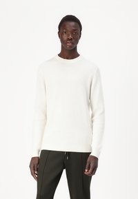Maglione bianco a coste con scollatura a girocollo, maniche lunghe e silhouette aderente, abbinato a pantaloni verde scuro.