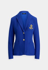 Blå blazer laget av teksturert stoff, med enkeltspent design, to frontlommer, gullknapper og en brodert logo på brystet.