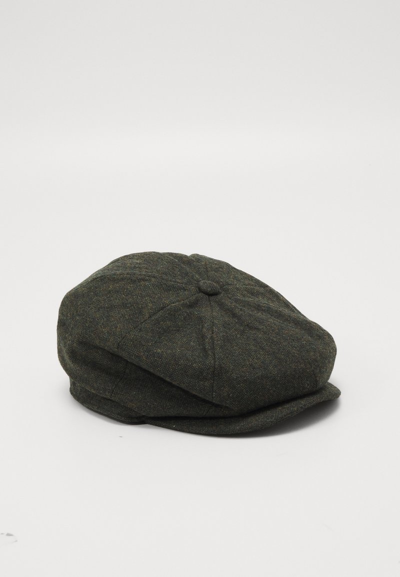 Casquette plate en laine vert foncé avec des panneaux cousus et un petit bouton sur le dessus, posée sur une surface blanche.
