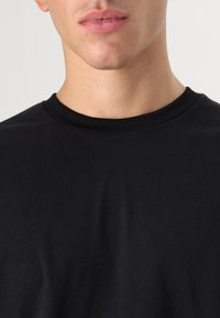 Sort bomulds t-shirt med rund hals. Glat tekstur og tætsiddende design, der dækker den øverste del af torsoen. Ingen synlige logoer eller indviklede detaljer.