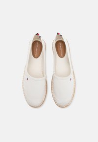 Valkoiset kangasespadrillot punotulla juttupohjalla, joissa on pieni logo päällisellä ja ruskea nahkainen sisäpohja, jossa on tuotemerkin nimi.