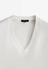 T-shirt blanc en coton avec col en V côtelé et étiquette de marque noire cousue à l’intérieur du col.