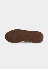 Suola marrone di scarpa Adidas con battistrada decorato con esagoni, linee a zigzag e logo Adidas impresso al centro.
