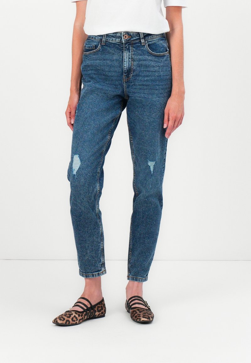 Jean bleu taille haute avec détails déchirés, dotés d'un design classique à cinq poches et d'une jambe fuselée. Associés à des ballerines à imprimé léopard.