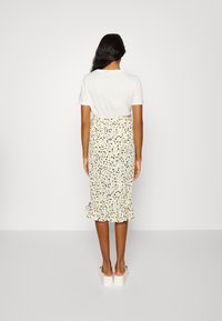 Witte korte mouwen blouse gecombineerd met een gele kokerrok met bloemenprint en een geplooide zoom, gedragen met lichtgekleurde instapschoenen.