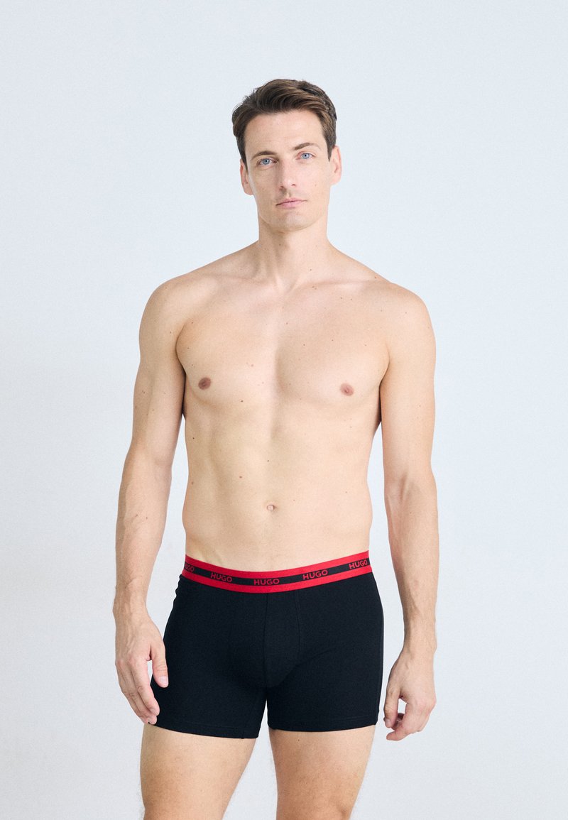 Schwarze Boxer-Briefs mit rohem elastischem Bund, der das Branding "HUGO" trägt, designed für eine enge Passform und aus weichem Stoff gefertigt.