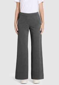 Graue weite Hosen aus weichem, dehnbarem Stoff mit einem glatten Bund und seitlichen Taschen. Modell trägt weiße Sneaker.