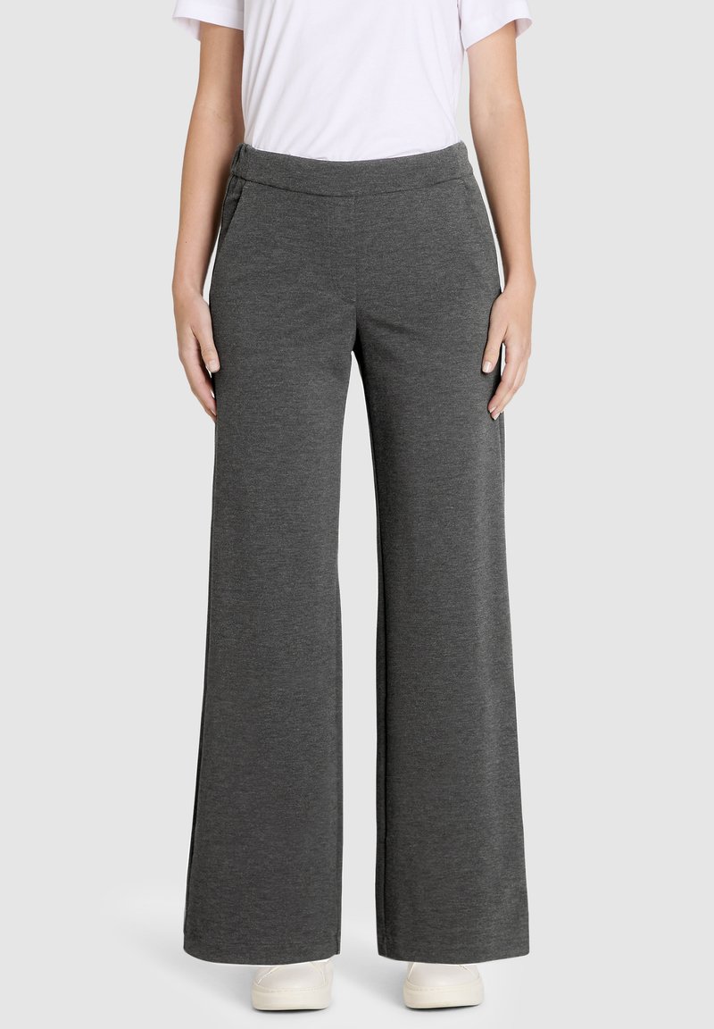 Graue weite Hosen aus weichem, dehnbarem Stoff mit einem glatten Bund und seitlichen Taschen. Modell trägt weiße Sneaker.