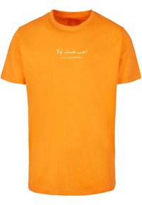 Oranžinės medvilninės marškinėliai su apvaliu kaklu ir trumpomis rankovėmis. Tekstas skaito "أحب نفسك أولاً - Love yourself first -" balta spalva.