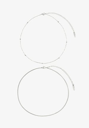 Dos cadenas de plata: la cadena superior tiene acentos de cuentas redondas y un cierre de langosta; la cadena inferior tiene un diseño liso y plano con un cierre simple.