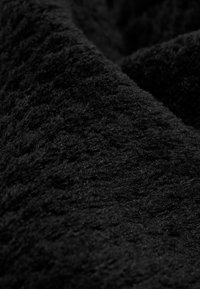 Tessuto nero con una superficie morbida e strutturata, che presenta un pelo profondo e una leggera lucentezza, disposto in morbide pieghe e contorni.