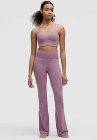 Set atletico di un leggero viola composto da un top corto con spalline sottili e pantaloni a vita alta svasati, realizzati in un materiale liscio ed elastico.