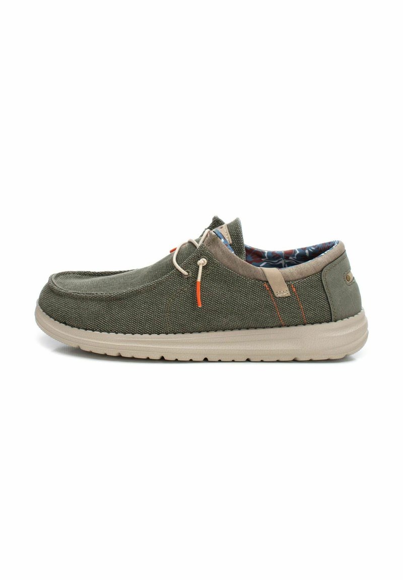Zapatilla de lona verde sin cordones con suela beige, que presenta acentos naranjas y un forro interior estampado. Textura ligera, diseño casual.