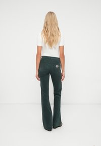 Roheline kangaskrutsidega flared teksapüksid kõrge vöökoht, tagataskud ja logopatch; koos slim-fit valge lühikeste varrukatega topiga.