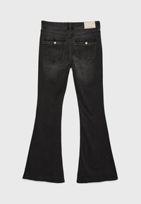 Jeans negros de campana con un acabado desgastado, que cuentan con dos bolsillos traseros, herrajes plateados y una cinturilla lisa con una etiqueta blanca.