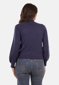 Maglione blu navy con un design aderente, maniche lunghe a palloncino e un collo alto, abbinato a jeans denim aderenti.