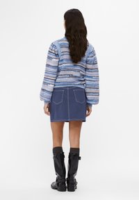 Niebieski sweter w paski z dzianiny z bufkami na rękawach, zestawiony z ciemną spódnicą dżinsową. Czarne kozaki za kolano z klamrami dopełniają strój.