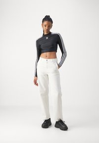 Top preto cropped de manga longa com três riscas brancas e um pequeno logótipo, combinado com jeans brancos de perna reta e ténis pretos.