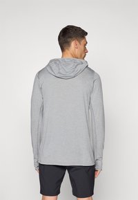 Langermet grå hettegenser laget av mykt stoff, med hette, sømløse skuldre og en avslappet passform, sammen med mørke shorts.