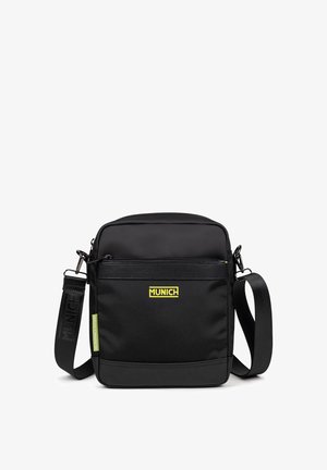 Sacoche en tissu noir avec une bandoulière réglable, poche zippée à l'avant et logo "MUNICH" jaune. Design compact et carré avec une texture lisse.